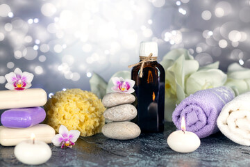 Fototapeta na wymiar Massage stones, natural sea sponge, seashell, burning candles, rolled towels, soap, massage oil, sea salt, flowers, abstract lights. Spa resort therapy composition
