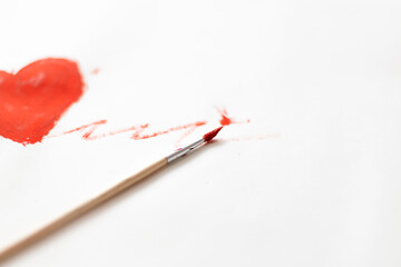 A brush in red paint lies on a white sheet of paper. A red line drawn by a brush on a white background.