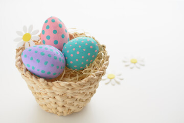 Easter eggs with colored spots, in a wooden basket, with white background and white flowers