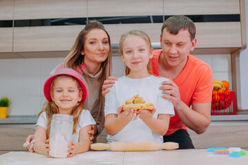 Mom with Father teaches two daughters to cook dough in the kitchen.