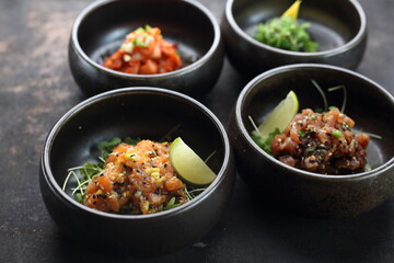 Salmon tartare, tuna tartare, on a black stony background. A composition of appetizers.