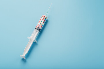Syringe filled with colorful nano balls on a light blue background.