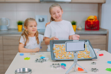 Two sisters bloggers are making cookies and filming training videos on a smartphone.