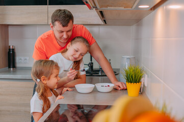 A father feeds his daughters in the kitchen on a background of fruits.