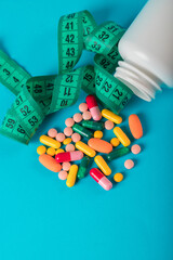 Diet concept. Slim by pills, dangerous for health. Centimeter tape and pills on a colored...