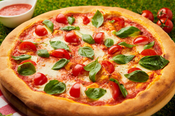 Traditional italian Pizza margarita with cheese, tomato and basil on green grass background