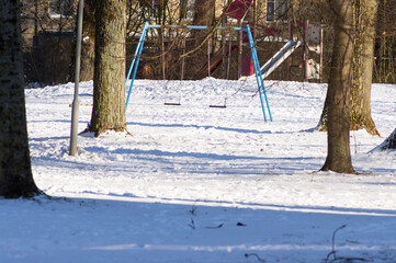 Swing at playground for children in a public park in winter with snow