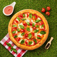 Traditional italian Pizza margarita with cheese, tomato and basil on green grass background