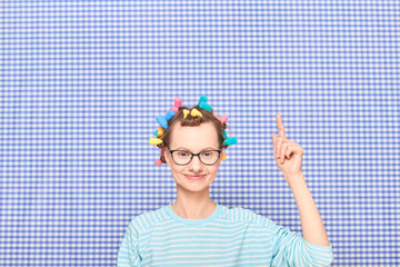 Cute girl with colorful hair curlers on head is pointing at copy space
