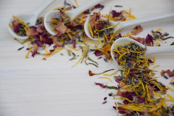 Colorful dry herbs on white ceramic  spoons, white wooden background with space for text