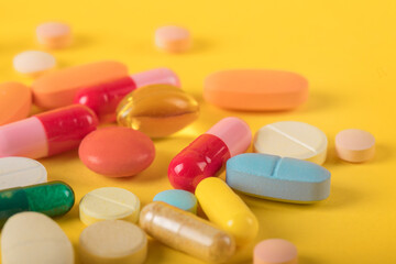 Assorted pharmaceutical medicine pills, tablets and capsules over yellow background. High number of pills on  surface. High resolution image for pharmaceutical industry.