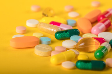 Assorted pharmaceutical medicine pills, tablets and capsules over yellow background. High number of pills on  surface. High resolution image for pharmaceutical industry.