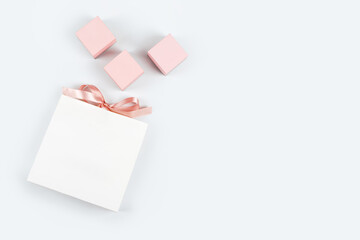 White paper shopping bag with bow and three pink gift boxes on light background. Shopping, sale, gift theme