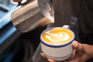Closed up of barista’s hand pouring milk froth to make latte art in white ceramic cup