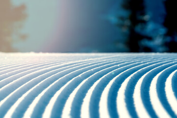 Close up of groomed tracks on a slope in a downhill ski resort on a sunny day. Shallow depth of...