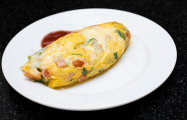 Omelet with cheese ham and vegetables. Serving with tomato sauce on white plate. Traditional breakfast of English style or American style