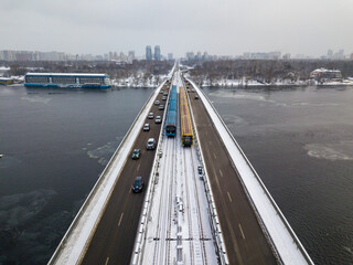 Two metro trains on a snow-covered metro bridge in Kiev. Cloudy winter morning. Aerial drone view.