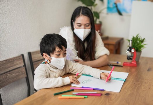 Asian mother drawing with little kid at home while wearing surgical face masks for coronavirus outbreak - Mother and child love