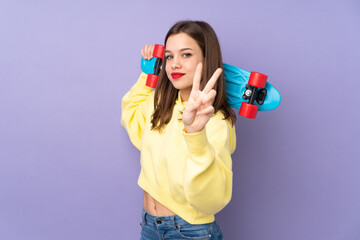 Teenager girl isolated on purple background with a skate doing victory gesture © luismolinero