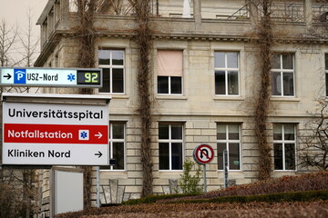 Zurich, Switzerland - 02 06 2021: Signpost of Emergency room or E.R. direction at University Zurich Hospital and adjacent parking lot. Directions are all written in German language.