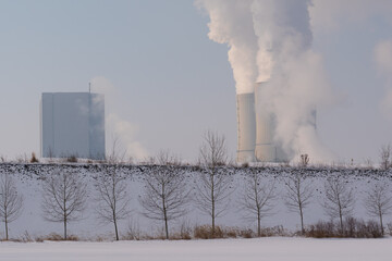 Snowy landscape with blue sky and sunshine, in the background a coal-fired power station and smoke