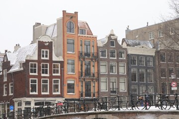 Fototapeta premium Torensluis Street View with House Facades, Bridge Railing, Parked Bicycles and Snow in Amsterdam, Netherlands