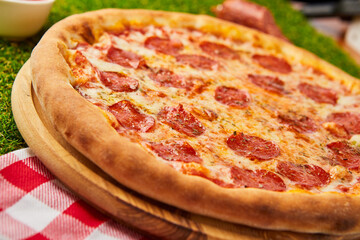 Traditional italian Pizza Pepperoni with salami, mozzarella and basil on green grass background