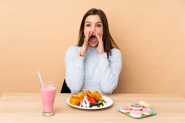 Teenager girl eating waffles isolated on beige background shouting and announcing something