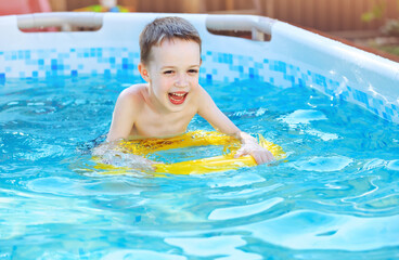 Fototapeta na wymiar Little boy is splashing with inflatable toy in swimming pool outdoor, having fun. Kids learn to swim