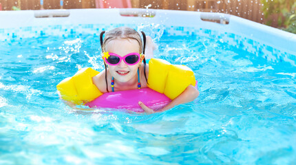 Fototapeta na wymiar Little girl is splashing in frame swimming pool outdoor at home garden