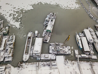 Aerial drone view. Cargo ships in a frozen bay. Cloudy frosty winter morning.
