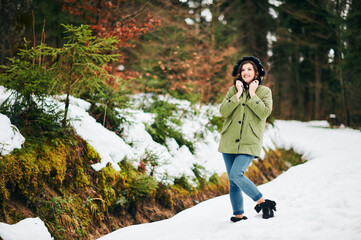 Warm winter portrait of happy young woman hiking in forest, wearing green fashion parka