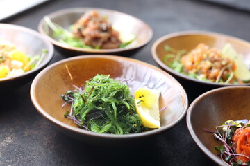 Japanese seaweed salad on a black stony background, a composition of appetizers in a background.