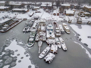Aerial drone view. Cargo ships in a frozen bay. Cloudy frosty winter morning.