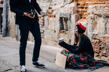 Man in tuxedo came up to beggar to help, give money donation. Rich man hold out his hand with money to homeless person. People relationship concept