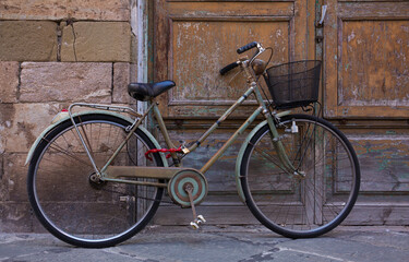 Fototapeta na wymiar An classic, old, vintage bicycle with wicker basket rests against a weathered wall and door in Lucca, Italy 