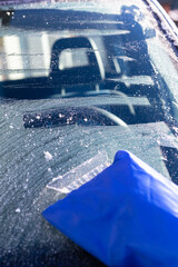 Scraping ice from frosted car window early in sunny morning