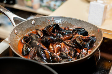 Mussels in a cream and white wine sauce are cooked on the stove in a wok pan. Selective focus