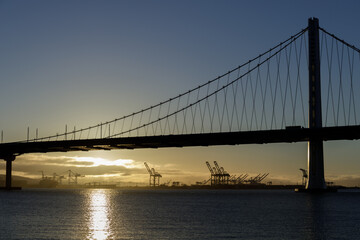 Sun rising behind the San Francisco-Oakland Bay Bridge Eastern Span and above Port of Oakland. Treasure Island, San Francisco, California, USA.