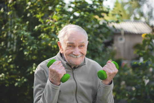 Old Man With Dumbbells. The Fitness Of The Person Engaged In In The Garden. Active Old Age, Healthy Lifestyle