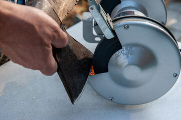 Close-up of men's hands sharpening an axe on an electric sharpener. Repair of home tools with Your...