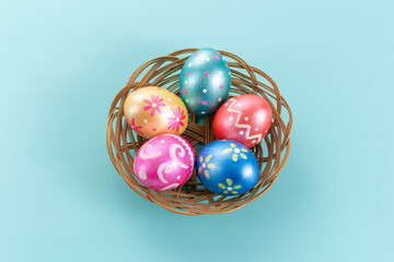 Five easter eggs trendy colored deep blue, green, orange, magenta and golden decorated in basket on blue background. Copy space for text.