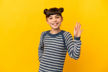 Little caucasian girl isolated on yellow background saluting with hand with happy expression