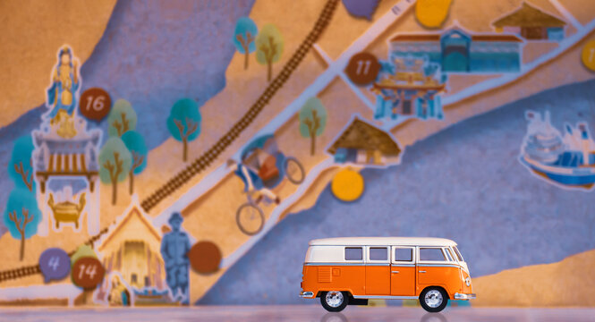 Samutsakhon, Thailand - February 07,2021: Mini Volkswagen van model on white floor with blurred tourist map board display of Tha Chalom district at Samutsakhon, creative idea for travelling concept