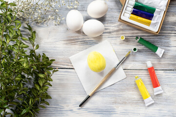 Painted yellow easter egg with paintbrush and paints on wooden table.