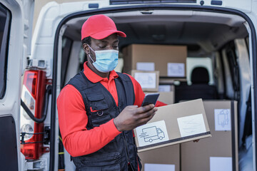 Young african delivery man with package and smartphone wearing surgical face mask for coronavirus outbreak