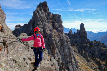 A young girl in bright sportswear walks along the Via Feratte in the Alps with a view of the beautiful mountains