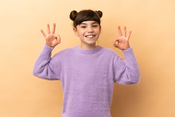 Little caucasian girl isolated on beige background showing ok sign with two hands