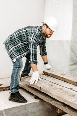 Man builder rearranges wooden beams at construction site
