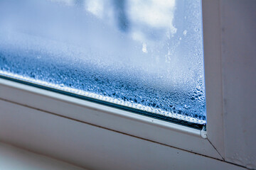 A fragment of a plastic window with condensation of water on the glass. Concept: defective plastic window with condensation, temperature difference, cooling, humidity in the room.